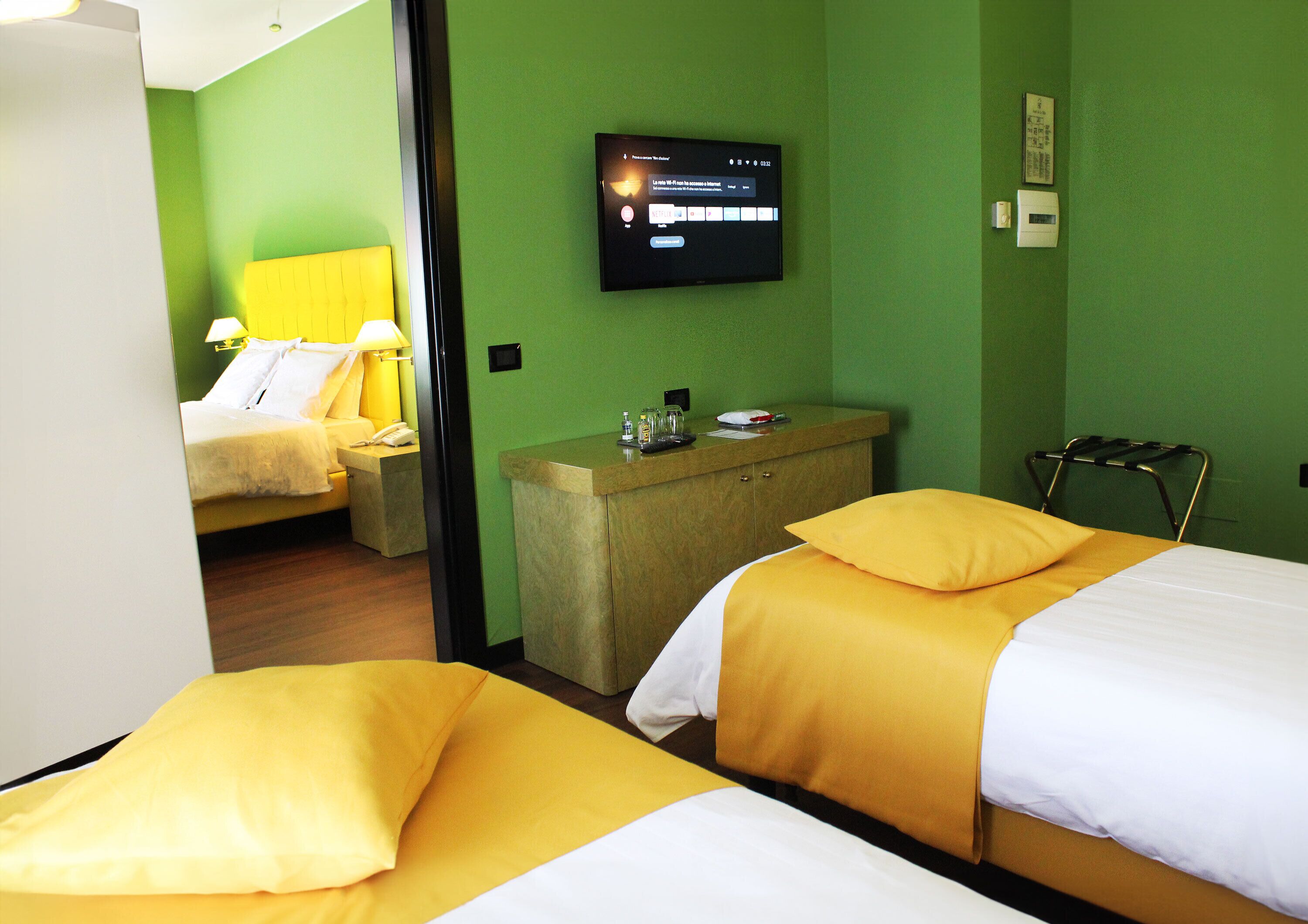 Camera d'albergo con due letti, una TV a muro, una piccola scrivania e una sedia.