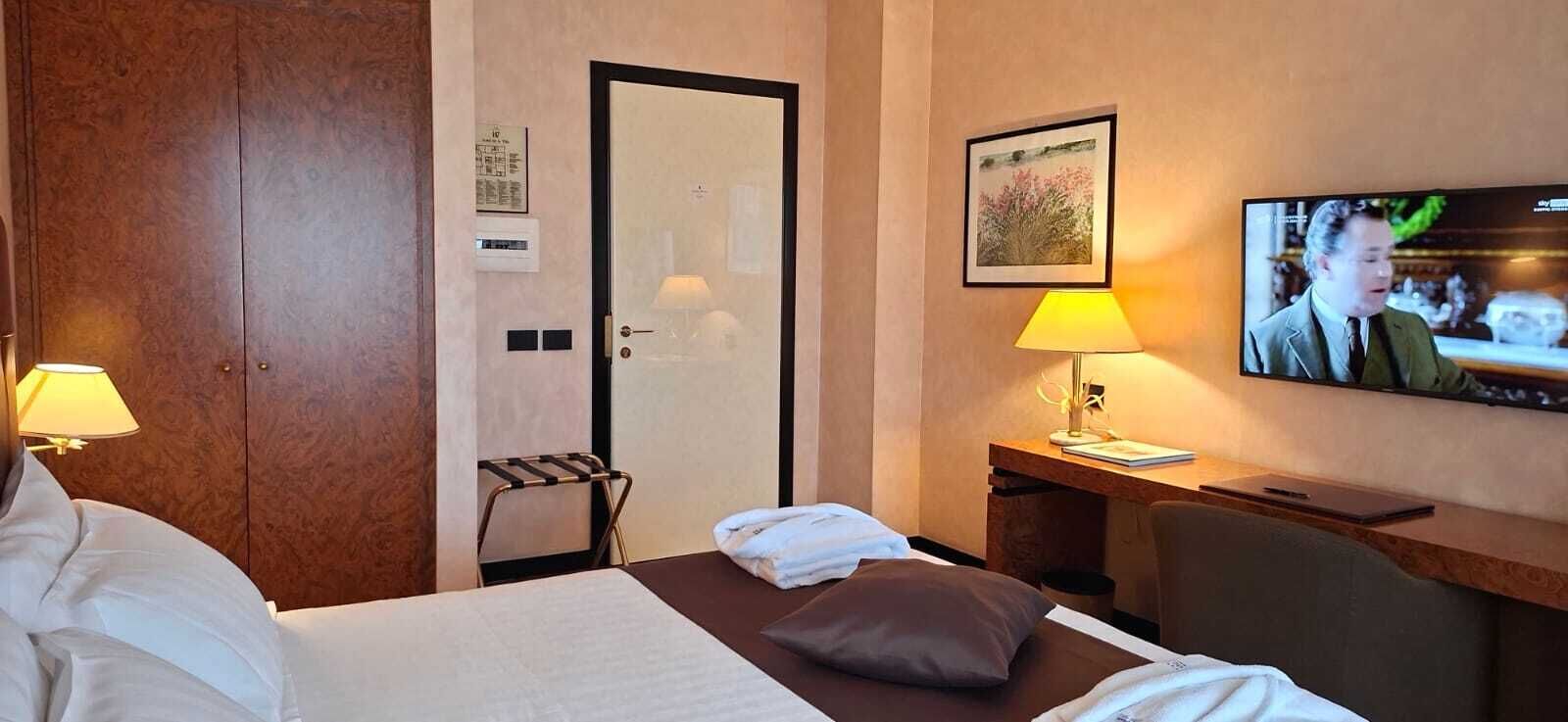 Une chambre d’hôtel avec un lit, des lampes de chevet, un bureau avec une télévision et une porte.