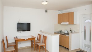A compact kitchen with a dining area, wooden cabinets, a built-in TV, and a small island. - Guest House Luce (Dubrovnik)