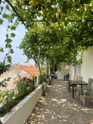 A covered outdoor patio with a table and chairs, surrounded by greenery and a white wall. - Guest House Luce (Dubrovnik)