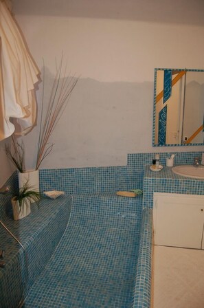 Een badkamer met vloeren en wanden van blauwe tegels, een witte wastafel, een spiegel met decoratieve lijst, en een handdoekrek.