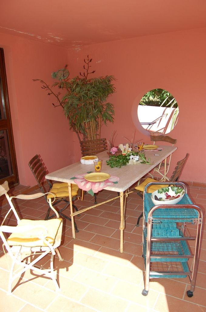 A dining area with a table set for two, surrounded by chairs, a potted plant, and a small mirror.