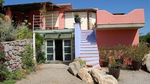Una casa de dos pisos con un muro de piedra, una escalera azul y plantas en macetas.