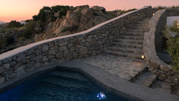 A stone staircase leading to a pool surrounded by rocks and vegetation. - Ikies of Mykonos (Mykonos)