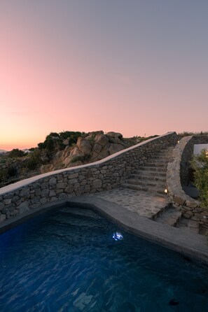 A stone staircase leading to a pool surrounded by rocks and vegetation. - Ikies of Mykonos (Mykonos)