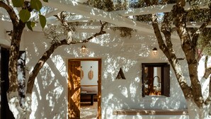 A white-walled room with a wooden bench, a bed, and a hanging light fixture. - Ikies of Mykonos (Mykonos)