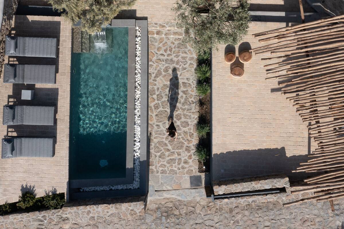 An aerial view of a rooftop pool area with stone flooring, lounge chairs, and a wooden deck.