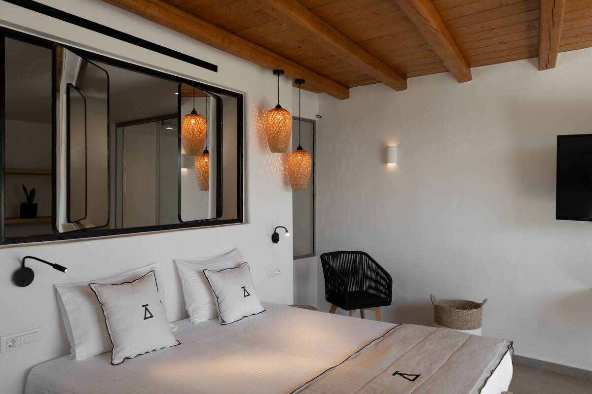 A modern bedroom with a large bed, a black chair, and a TV mounted on the wall.