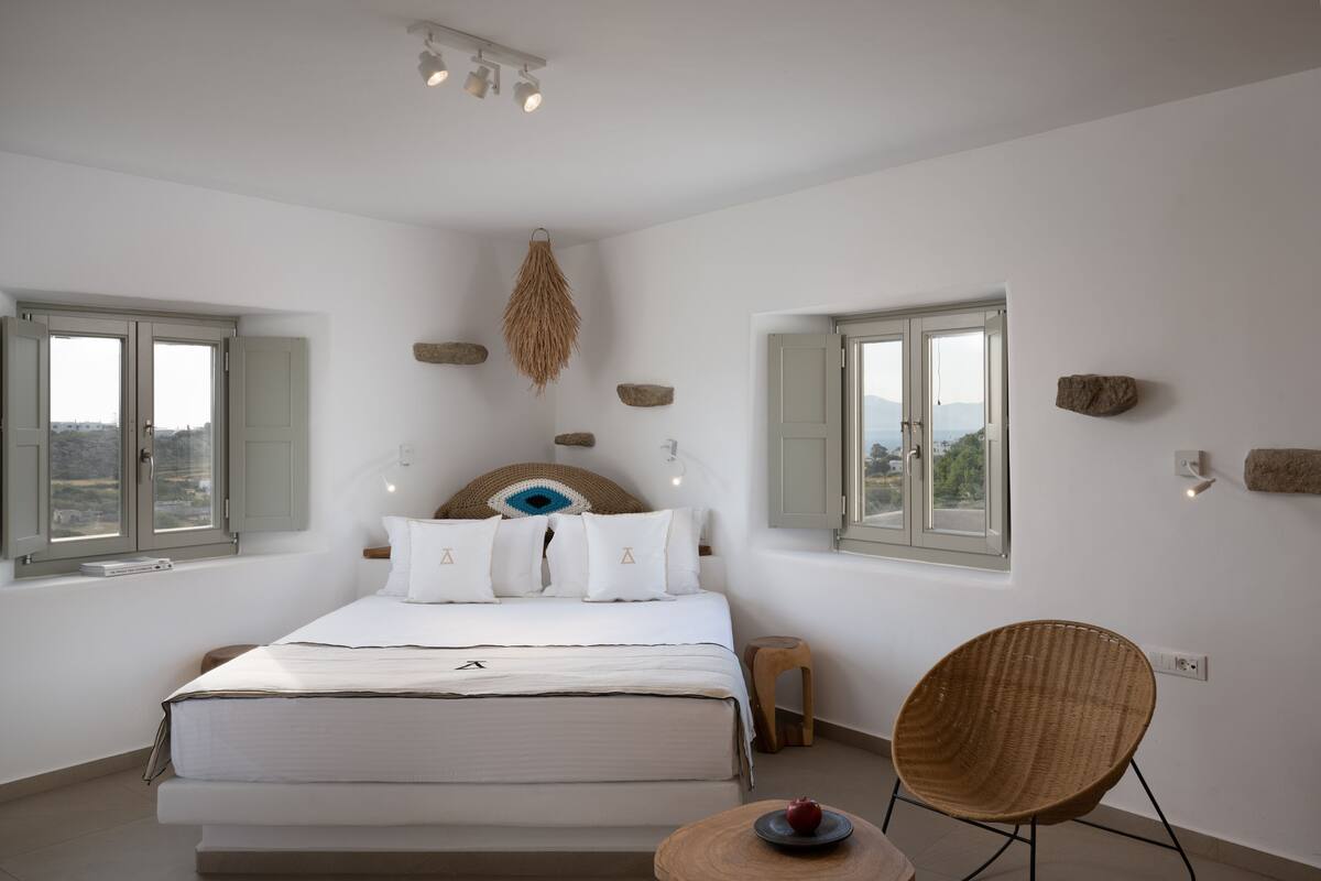 A bedroom with a bed, a chair, and a view through the windows.