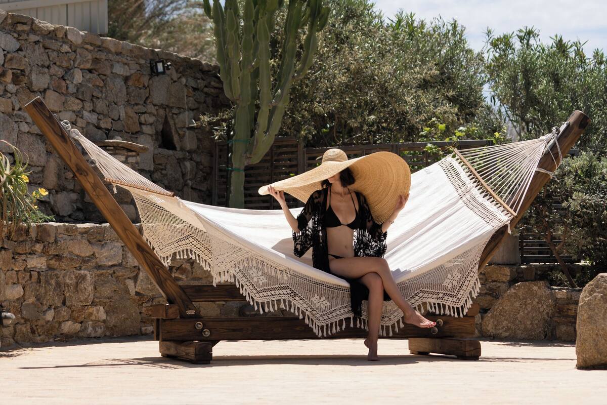 A hammock by a pool with a stone wall and cactus in the background.