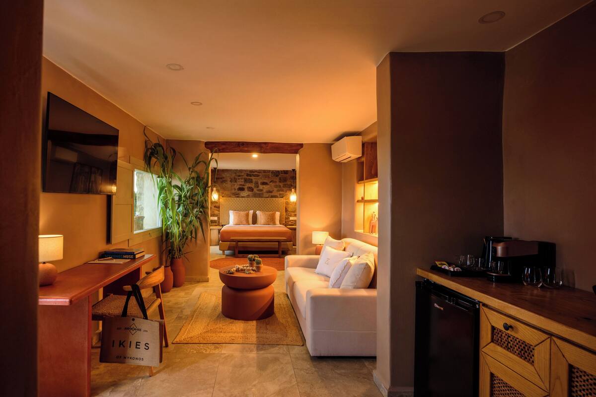 A cozy hotel room with a bed, a sofa, a dining area, and a kitchen.