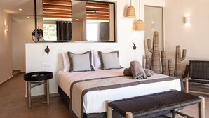 A bedroom with a large bed, a bedside table, a mirror, and a cacti decoration. - Ikies of Mykonos (Mykonos)