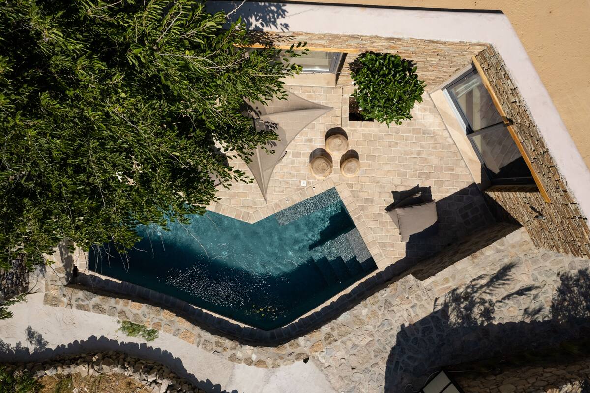 An aerial view of a swimming pool with a stone wall and a tree.