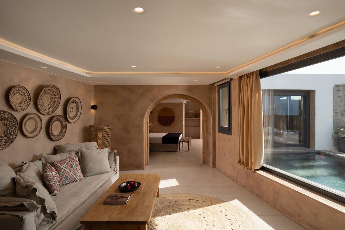 A modern living room with a sofa, coffee table, and decorative wall art. There is a view of a pool through a large window.