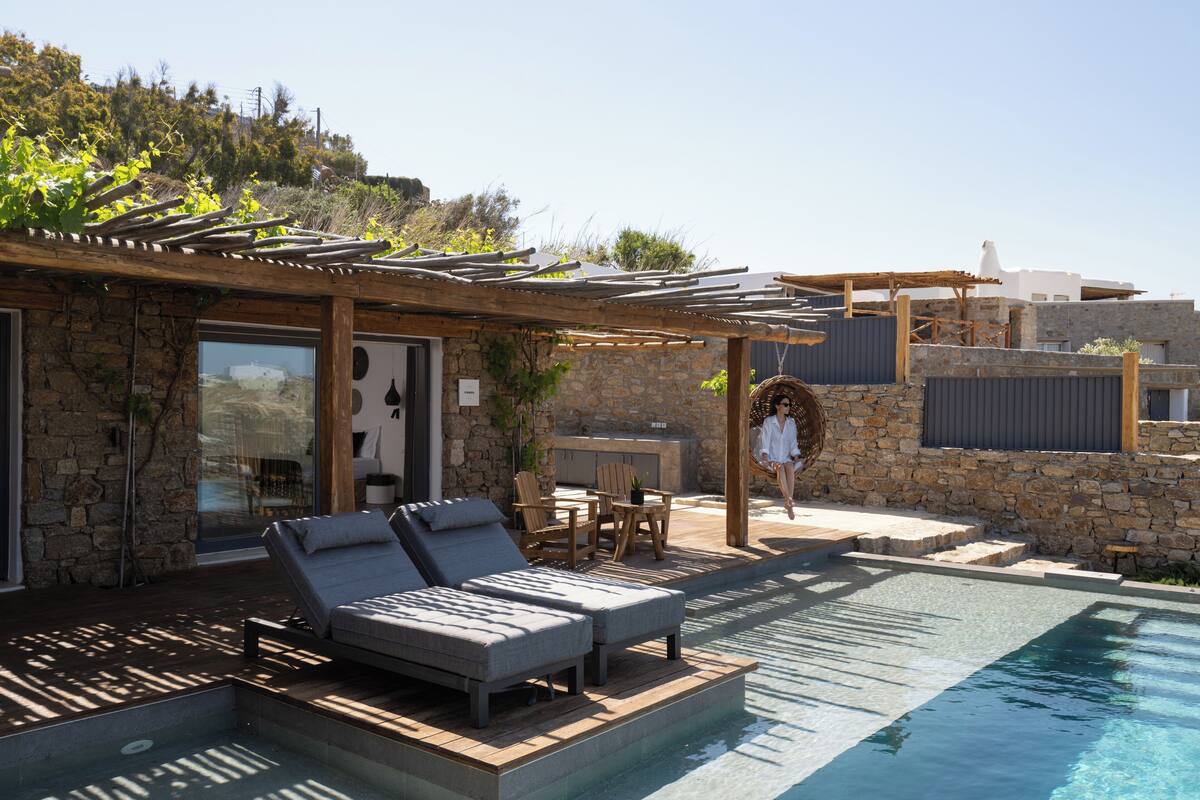 A poolside area with lounge chairs, a pergola, and a stone building.