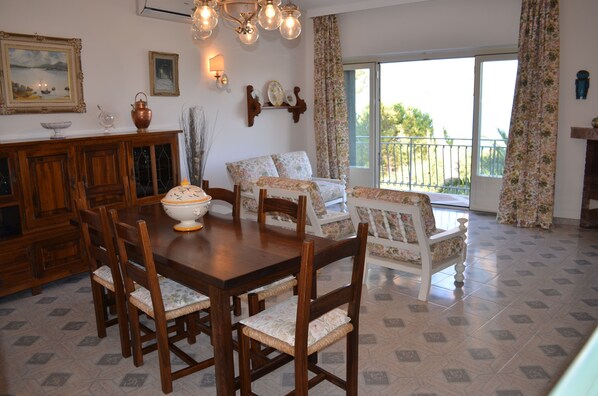 A dining area with a wooden table and chairs, a floral sofa, and a balcony with a view.
