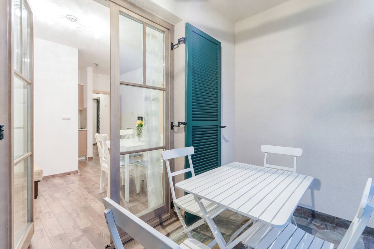 Ein kleiner Innenhof mit weißem Tisch und Stühlen, einer grünen Rolltür und Blick ins Innere des Gebäudes.