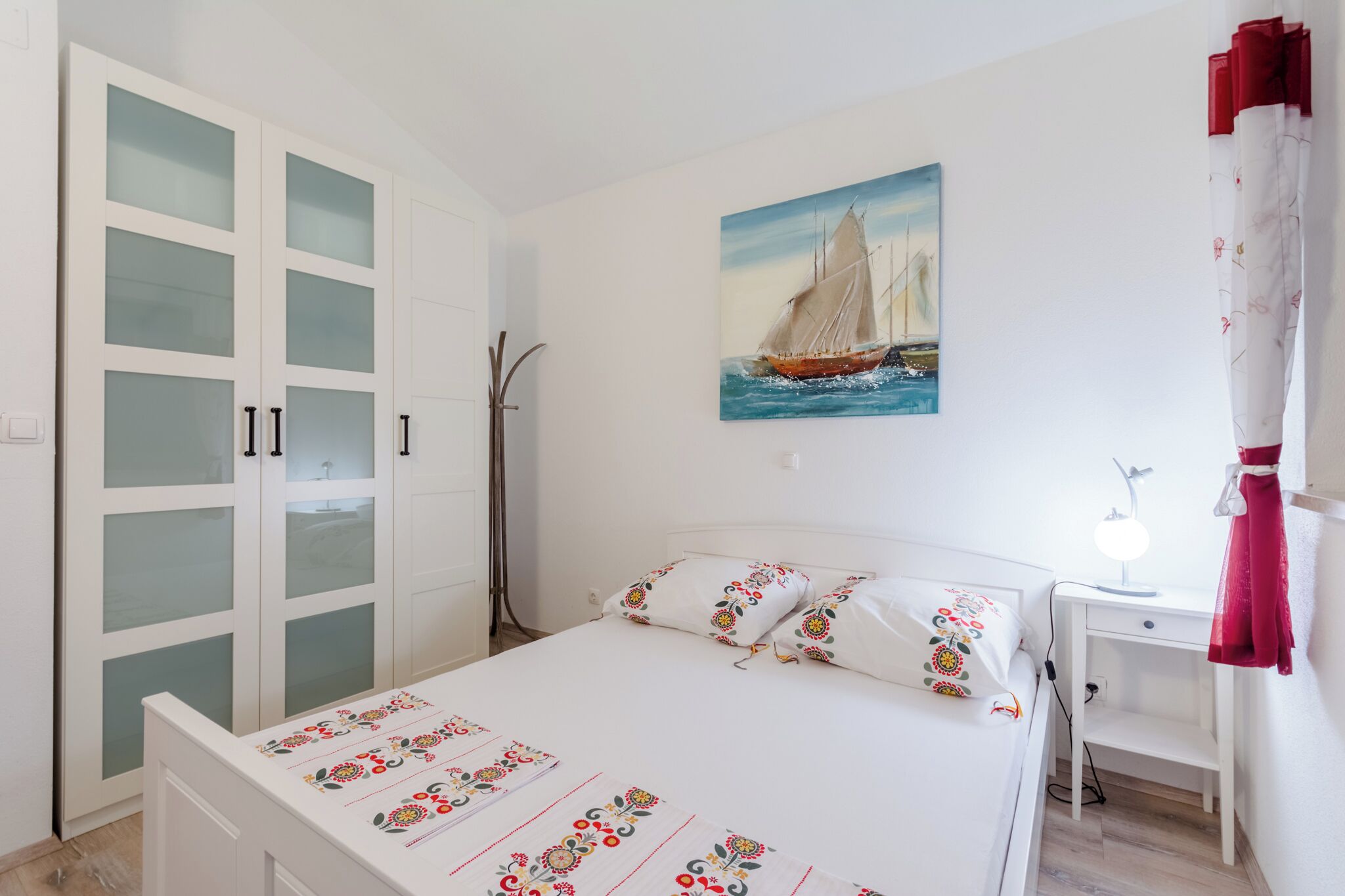 A bedroom with a bed, a desk, a chair, a wardrobe, and a painting on the wall.