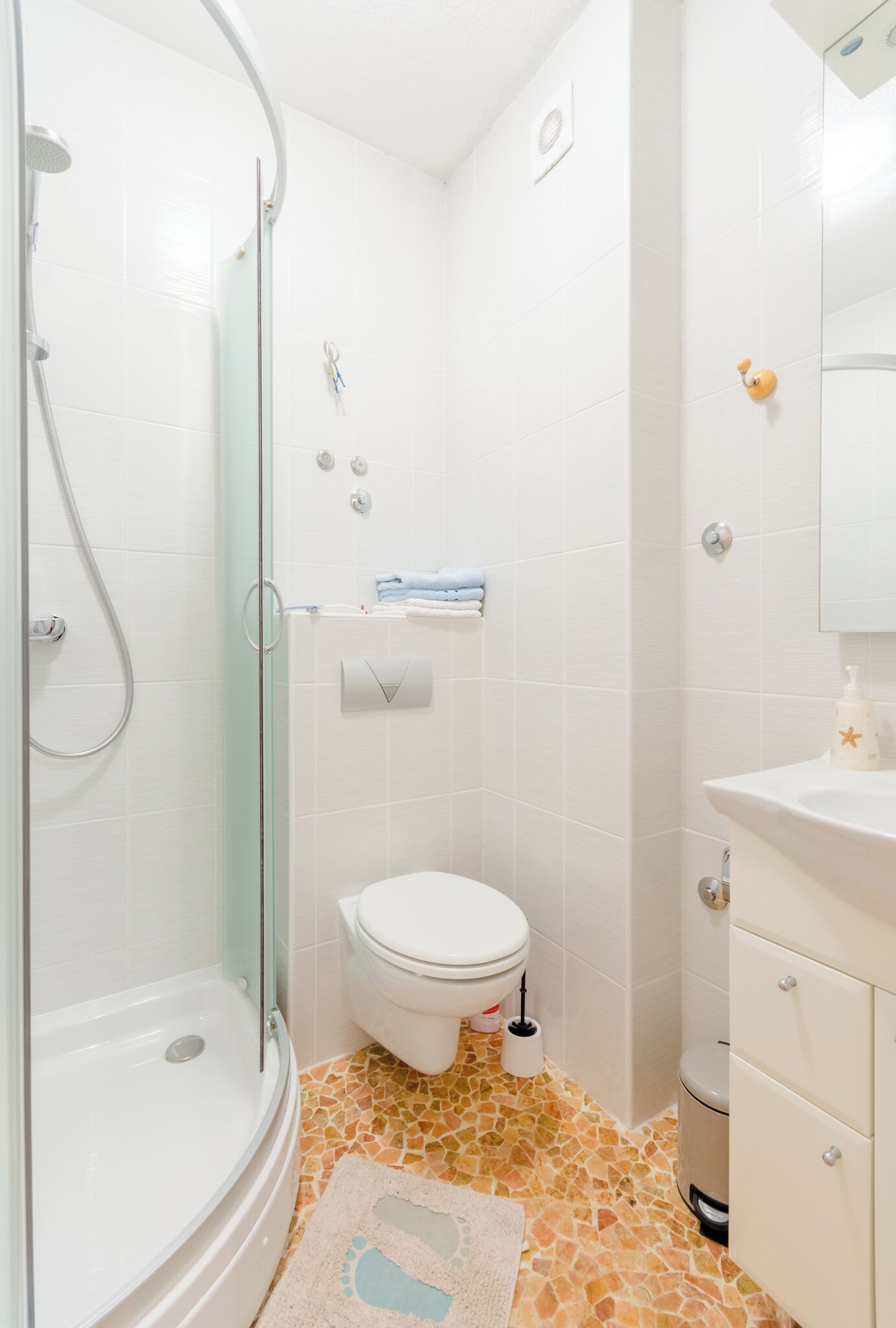 A bathroom with a glass-enclosed shower, a toilet, a sink, and a tiled floor.