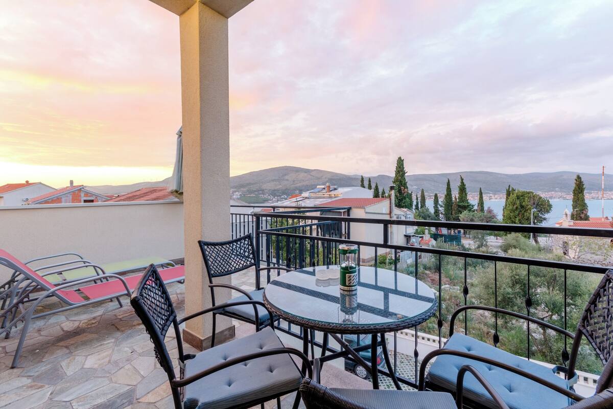 Ein Balkon mit rundem Tisch und Stühlen, der einen herrlichen Ausblick auf Berge und ein Gewässer bietet.