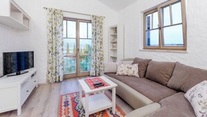 Ein Wohnzimmer mit einer Couch, einem Fernseher, einem kleinen Tisch und einem Fenster mit Vorhängen.