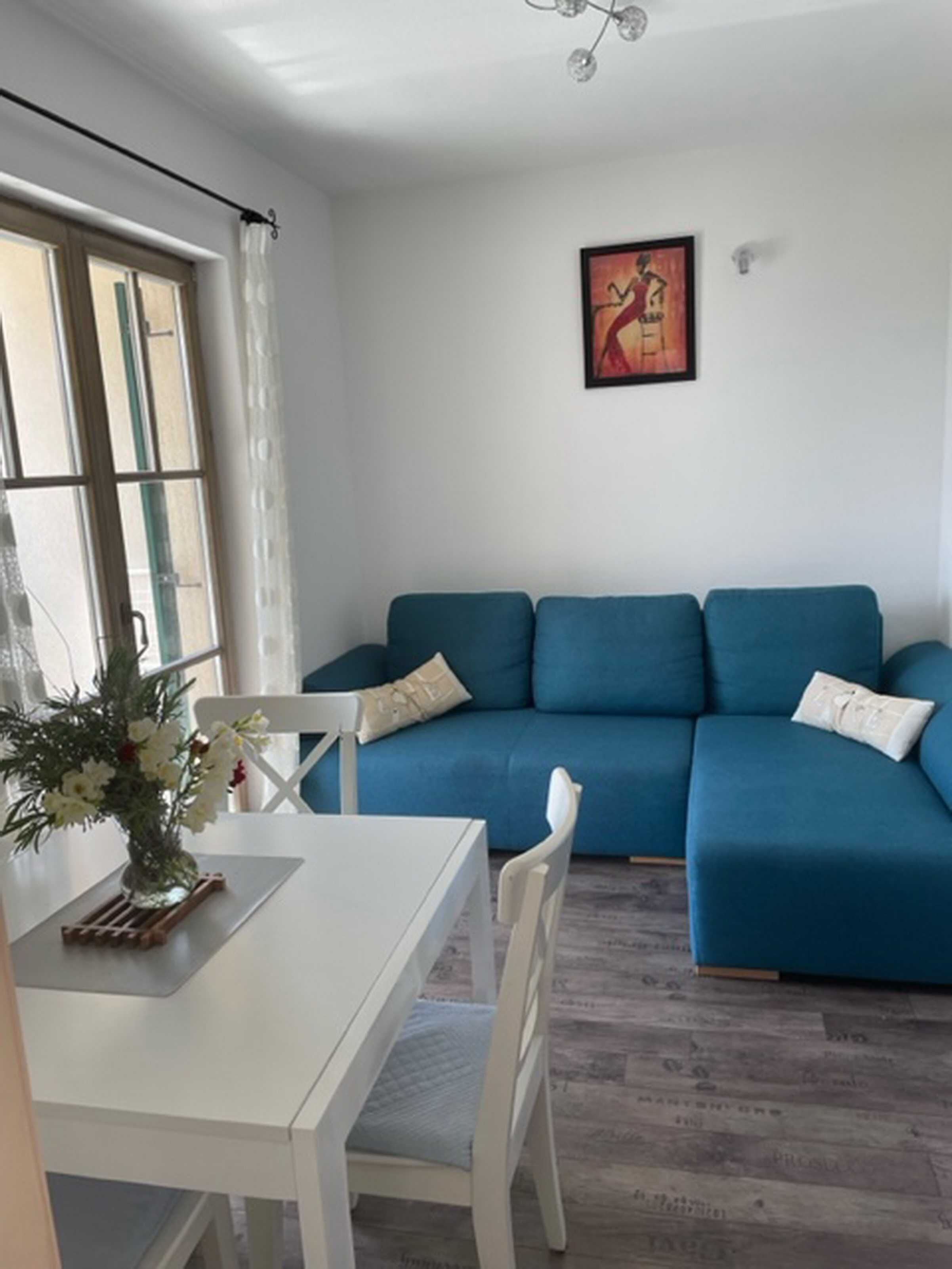 A living room with a blue sofa, white chairs, a white table, and a painting on the wall.
