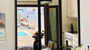 A room with a view of a pool and outdoor area, a dining table with chairs, a vase with flowers, and a kitchen area with cabinets and a stove. - Canaryislandshost l My Nest (Nazaret)