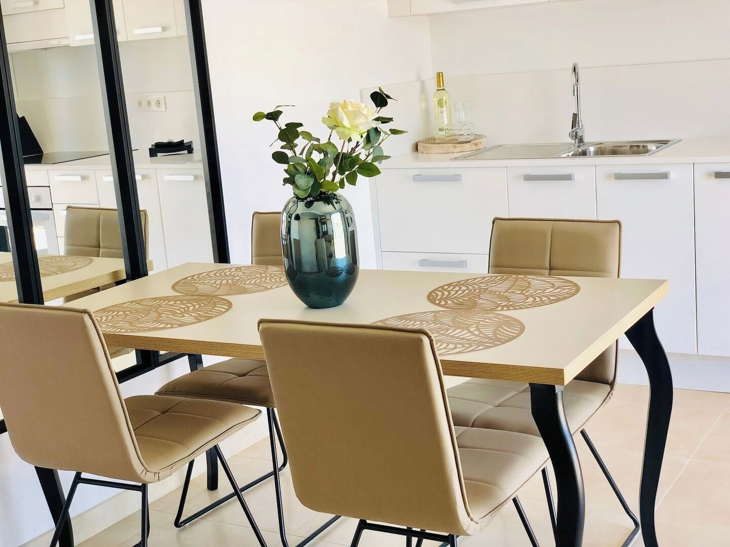 Un comedor moderno con una mesa rectangular, sillas color beige y un florero con flores.