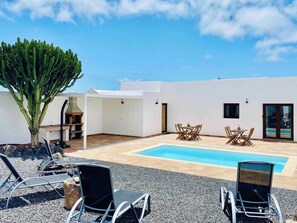 Zona de piscina en la azotea con sillones, una mesa y una gran planta de cactus.