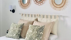 A bedroom with a white headboard, three wall-mounted mirrors with wooden frames, a black wall sconce, and two patterned pillows. - Canaryislandshost l My Nest (Nazaret)