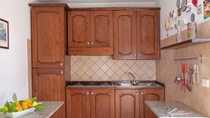 A kitchen with wooden cabinets, a granite countertop, and a stove. - Villetta dello Scrittore (Capoliveri)