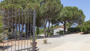A gated property with a gravel driveway, trees, and a stone building in the background. - Villetta dello Scrittore (Capoliveri)