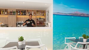 A bar area with a bartender, a seating area with white chairs and tables, and a view of a coastal landscape with mountains. - Mix Smart (Llucmajor)