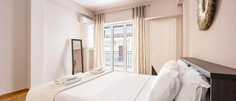 A hotel room with a large bed, a bedside table, a mirror, and a view of the outside.