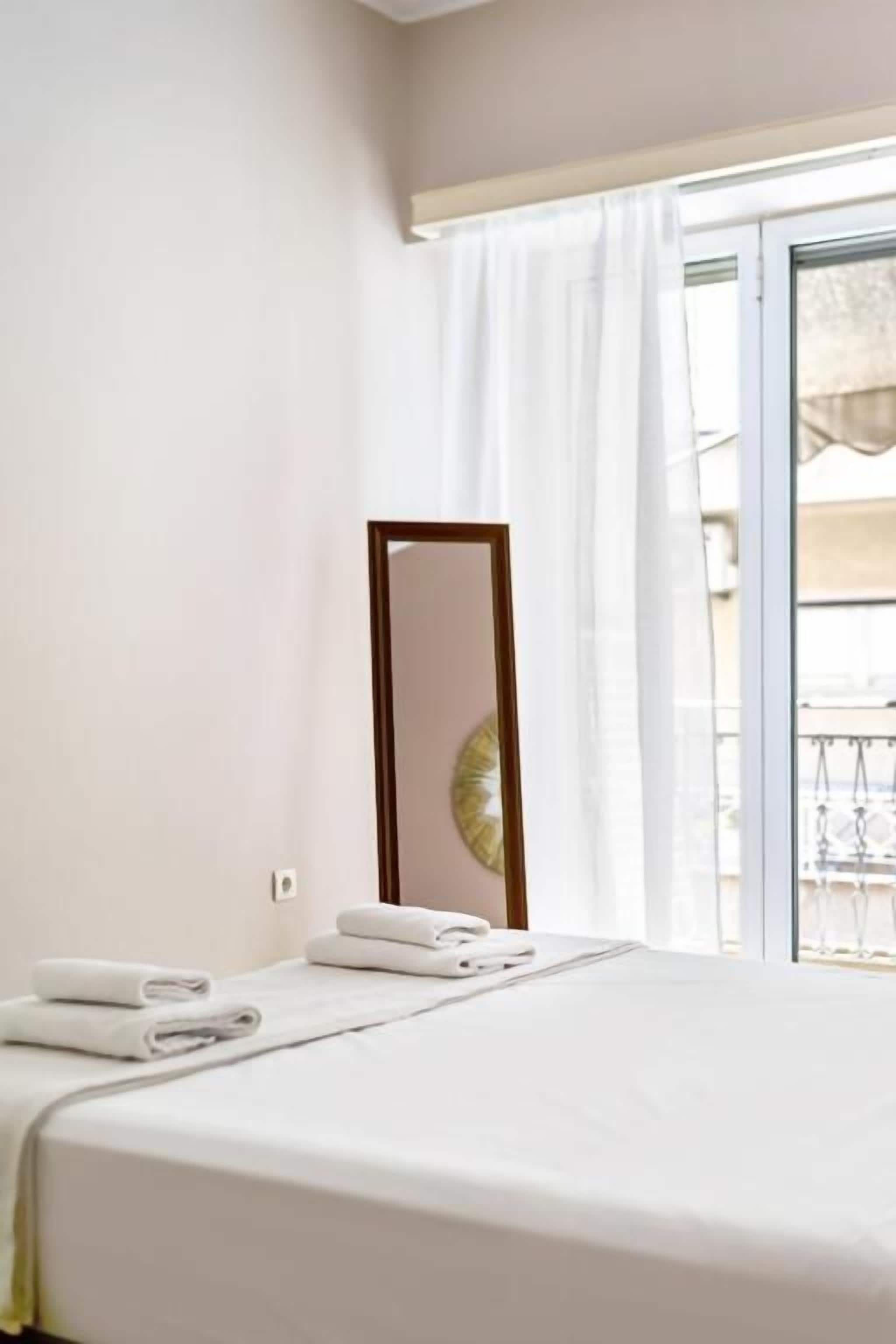 Habitación de hotel con cama, ventana con cortinas, espejo y vista al exterior.