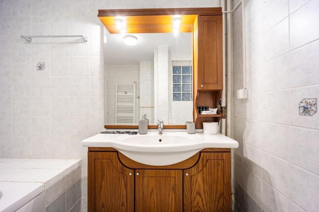 Un baño con tocador de madera, lavamanos, espejo y perchero para toallas.