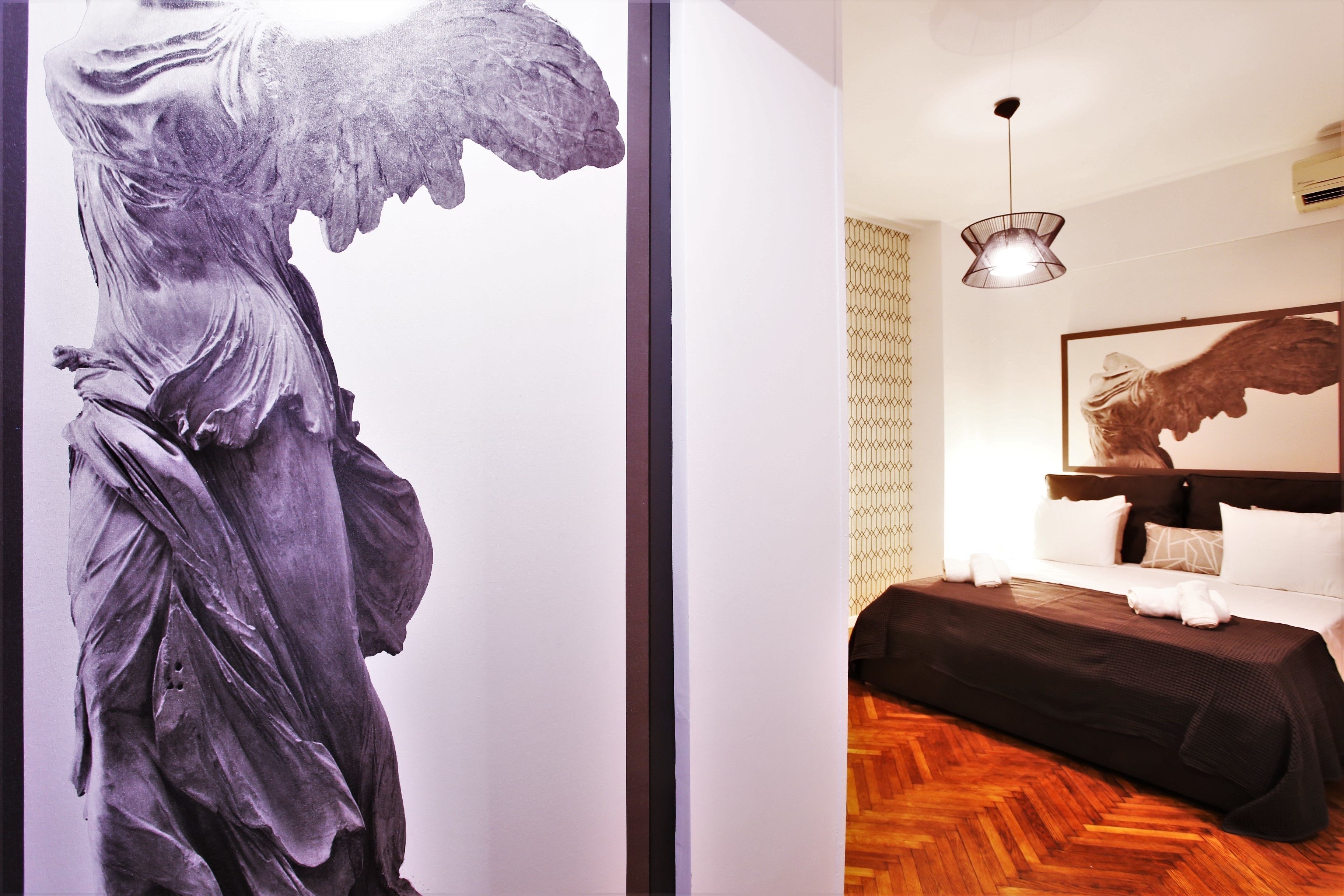 A room with a bed, a hanging light fixture, and a large artwork on the wall.