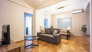 Un salon spacieux doté d’un parquet en bois disposé en chevrons, d’un canapé gris, d’une petite table ronde et d’un téléviseur posé sur un meuble en bois.