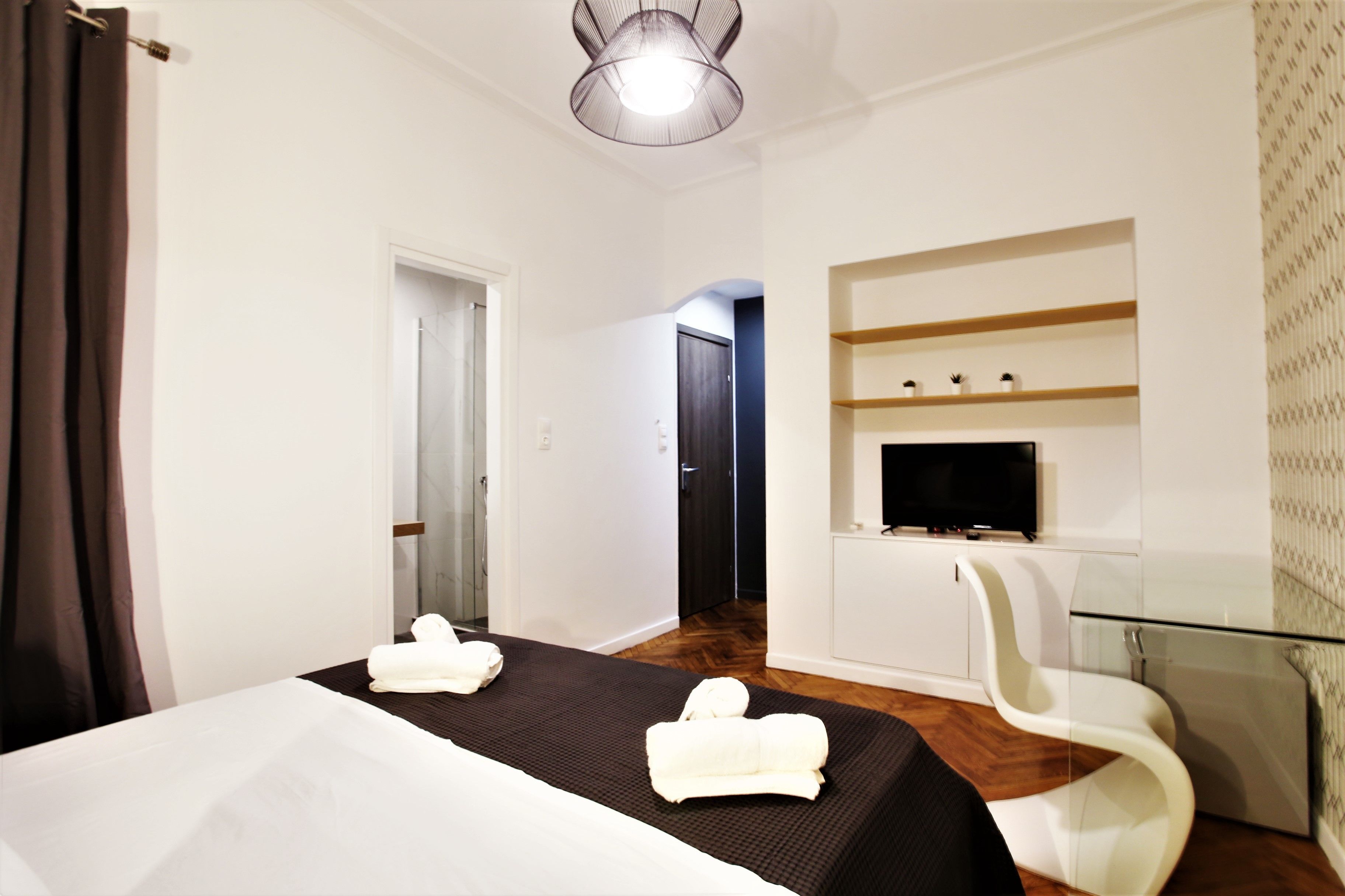 Una habitación de hotel con cama, televisor, una mesita de vidrio y una silla.