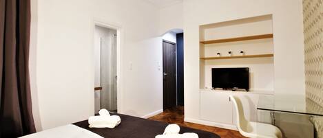 Una habitación de hotel con cama, televisor, una mesita de vidrio y una silla.