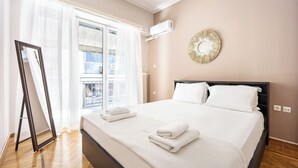 Un lit bien fait, avec du linge de lit et des serviettes blanches, une grande fenêtre avec des rideaux légers et un climatiseur fixé au mur.