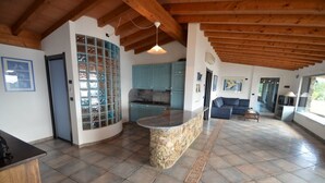 Un'ampia zona living con isola in pietra, una cucina con mobili blu e un'area pranzo con divano e tavolo.