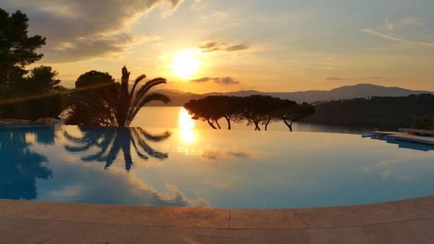 Una piscina tranquilla con il riflesso del tramonto, circondata da alberi e montagne lontane.