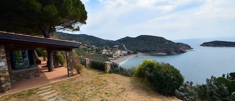 A coastal property with a stone building, a paved pathway, and a view of the sea and hills.