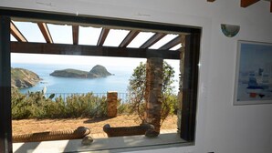 Una stanza con un'ampia finestra che si affaccia su un paesaggio costiero, colonne in pietra e un quadro appeso al muro.