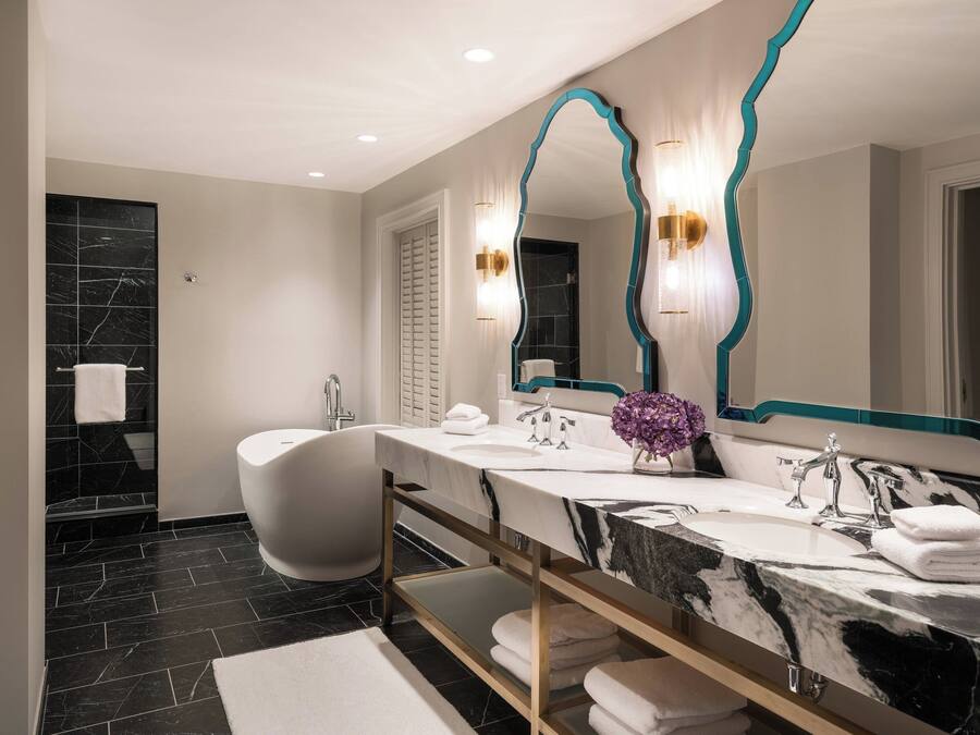 Un baño moderno con una bañera independiente, un tocador con encimera de mármol y un espejo grande con detalles en color turquesa.