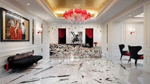 Un hall d’entrée spacieux avec un sol en marbre aux motifs géométriques, un canapé noir, un lustre rouge et un grand tableau accroché au mur.