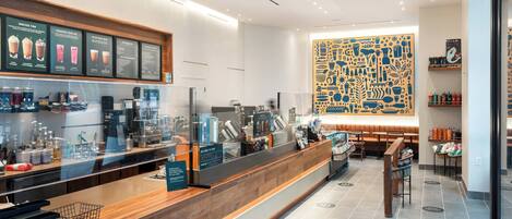 A modern hotel lobby with a wooden reception desk, a menu board, and a large abstract wall art piece.