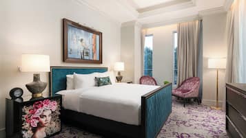 A hotel room with a large bed, two bedside lamps, a painting above the bed, a chair, and a view of the outdoors through a window.