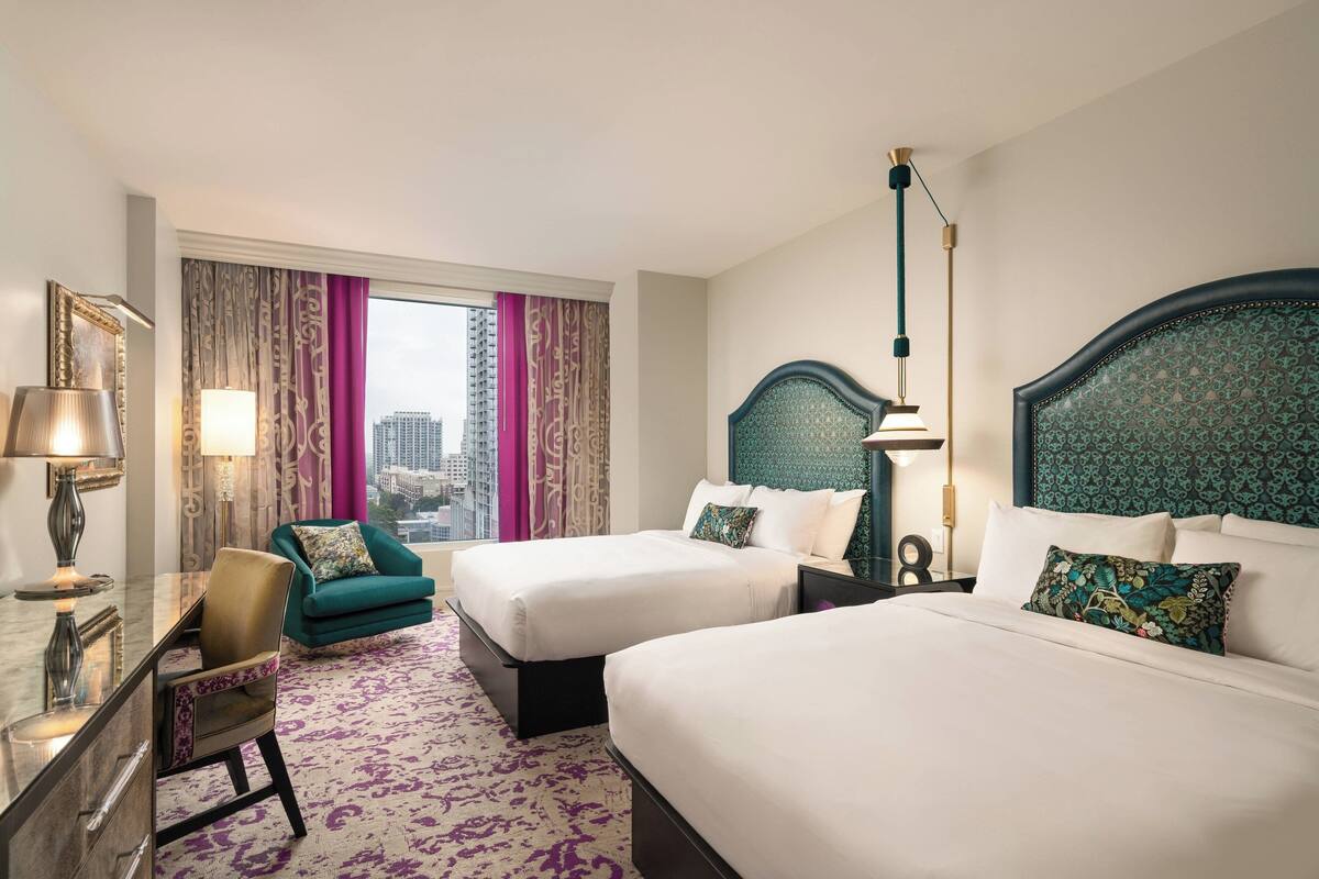 Ein Hotelzimmer mit zwei Betten, einem Schreibtisch, einem Stuhl und Blick auf die Stadt.